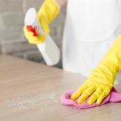 Hands wearing yellow rubber gloves cleaning a laminate tabletop.