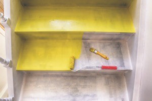 Paint roller and brush on half painted yellow cement stairs.