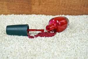 Bottle of red nail polish spilling on a beige carpet.
