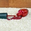 Bottle of red nail polish spilling on a beige carpet.