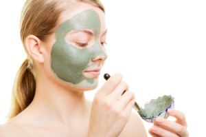 Woman applying green facial mask with a brush.