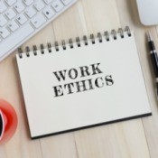 Keyboard, mug of coffee, pen and a notebook with the words "Work Ethics" printed on it.