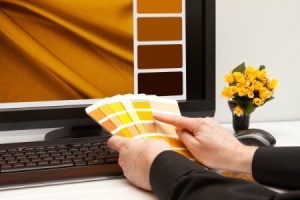 Person looking at paint chips in front of a computer showing color swatches.