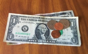 A pile of dollar bills and change on a wooden table.