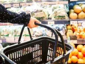 Person holding a shopping basket in font of the produce section.