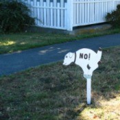 Yard sign of a dog pooping with "No!" painted on it.