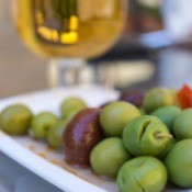 Plate of spiced olives with glass of white wine in background