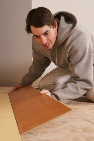 A man installing flooring on particle board.