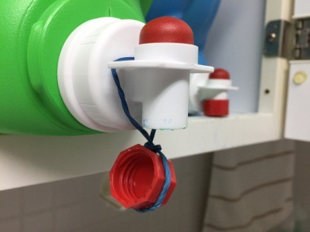 Laundry detergent dispenser with the lid hanging from a rubber band.