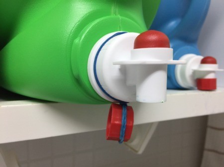 Laundry detergent dispenser with the lid hanging from a rubber band.