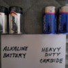 A set of alkaline batteries next to a set of heavy duty carbide batteries.