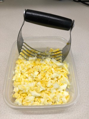 A pastry blender being used to chop up hard boiled eggs for egg salad.