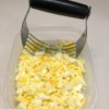 A pastry blender being used to chop up hard boiled eggs for egg salad.