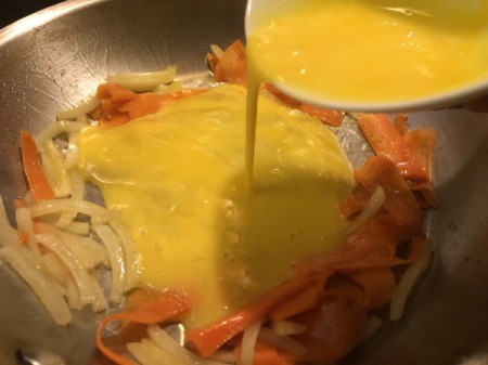 pouring egg on carrots and onion in pan