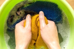 Hands washing a yellow sweater by hand.