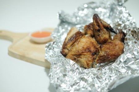 Baked chicken in aluminum foil on wooden cutting board