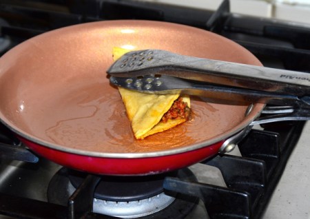 folded meat filled tortilla hed down with tongs