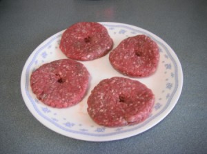 A plate of raw hamburger patties, with a hole in the center of each one.