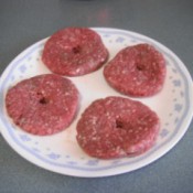 A plate of raw hamburger patties, with a hole in the center of each one.