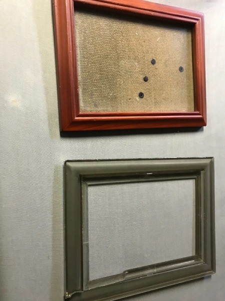 A broken picture frame underneath another frame that has had the glass replaced.