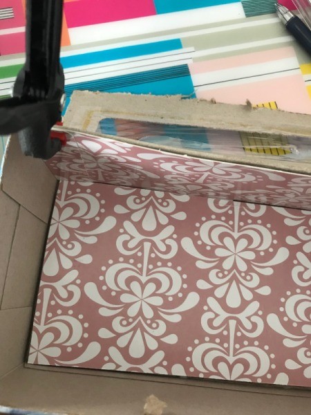 Coupon Organizer Made from a Tissue Box - looking down into the tissue box with bottom and back side covered with decorative cardboard - clip holding design paper in the upper left