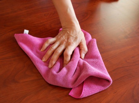 Hand using cloth towel to clean a wooden table