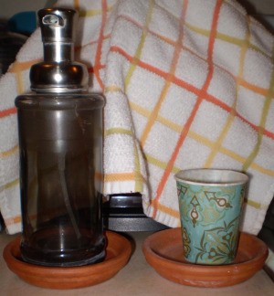 A soap dispenser and a water glass inside terra cotta planter bases.