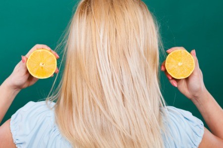 Back of a blonde haired person holding up a cut lemon next to their hair.