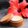 A wooden jar filled with lip balm and a pink flower on a wooden background.