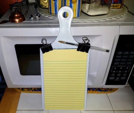 A small legal pad attached to a small cutting board with binder clips.