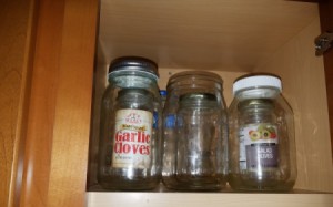 Small recycled glass jars stored inside larger jars in a cupboard.