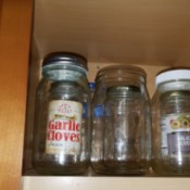 Small recycled glass jars stored inside larger jars in a cupboard.