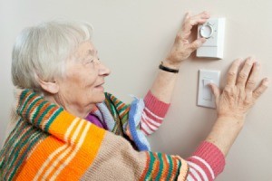 Elderly woman with a blanket around her shoulders adjusting her thermostat