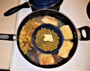 A pan cooking fish, potatoes and peas all at once.