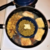 A pan cooking fish, potatoes and peas all at once.