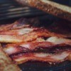 Bacon being cooked with slices of bread soaking up the grease.