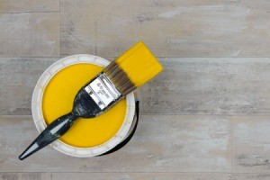 Wet paint brush with yellow paint on top of paint can