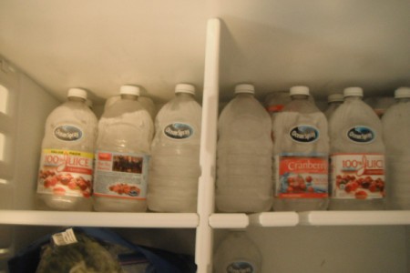 Recycled cranberry juice containers with water frozen and filling the back of a freezer.