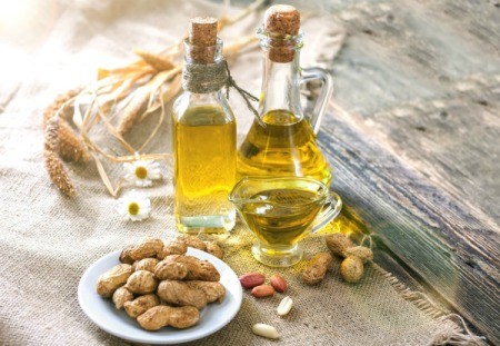Peanut oil in 2 glass bottles with a plate of peanuts.