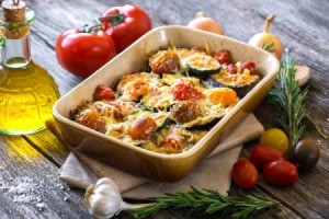 Eggplant And Zucchini Casserole on a wooden table with olive oil and other ingredients around dish