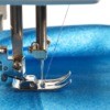 Sewing machine foot and needle on blue fabric.