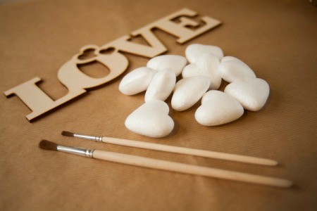 Styrofoam hearts with a wooden cutout of the word "love" and some paintbrushes.