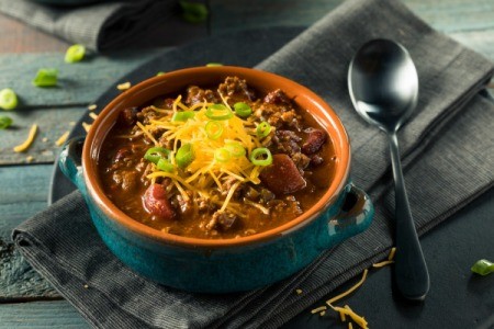 Chili in a bowl with grated cheese and a spoon on the side