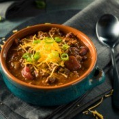 Chili in a bowl with grated cheese and a spoon on the side
