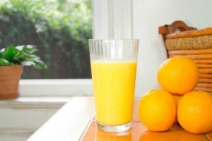 Orange juice in a glass next to a small stack of oranges