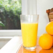 Orange juice in a glass next to a small stack of oranges