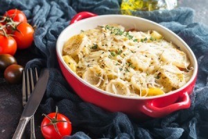 Scalloped potatoes in a red dish surrounded by tomatoes.