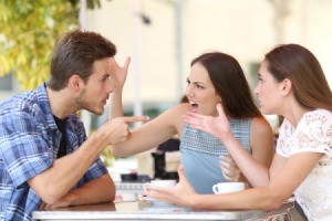 A male and two female arguing around an outdoor table.