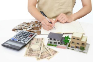 Woman calculating expenses, with money, calculator and a small house model.