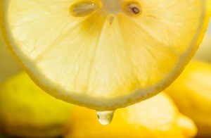 Close up of a slice of lemon, with one drop coming down.